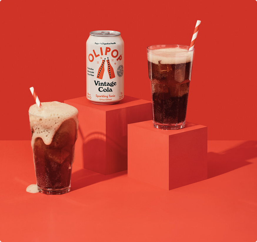 Three glasses of vintage cola with foam next to an OLIPOP can on red podium blocks